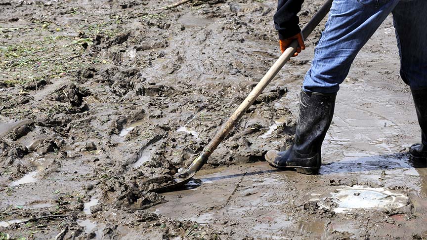 Person wearing gumboots and shovelling mud