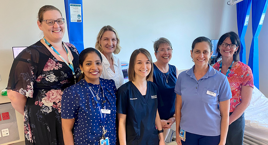 Group photo of seven women standing in hospital room smiling