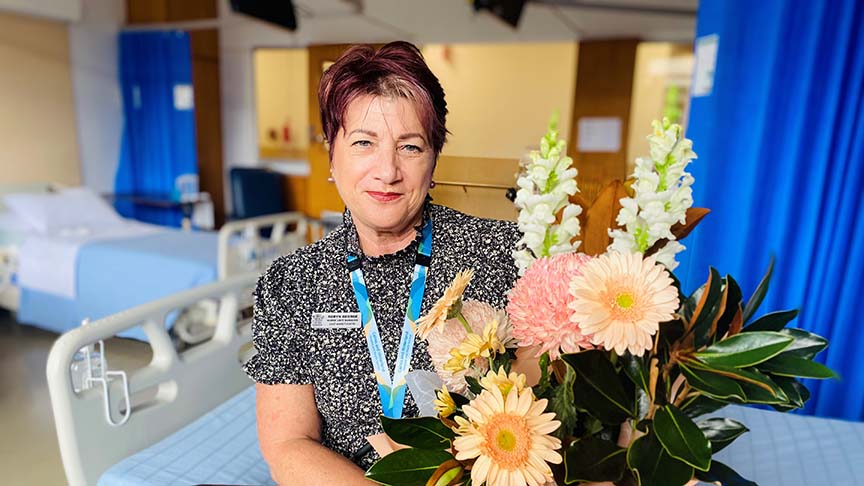 Woman (Nurse Unit Manager Robyn George) standing in hospital room holding flowers