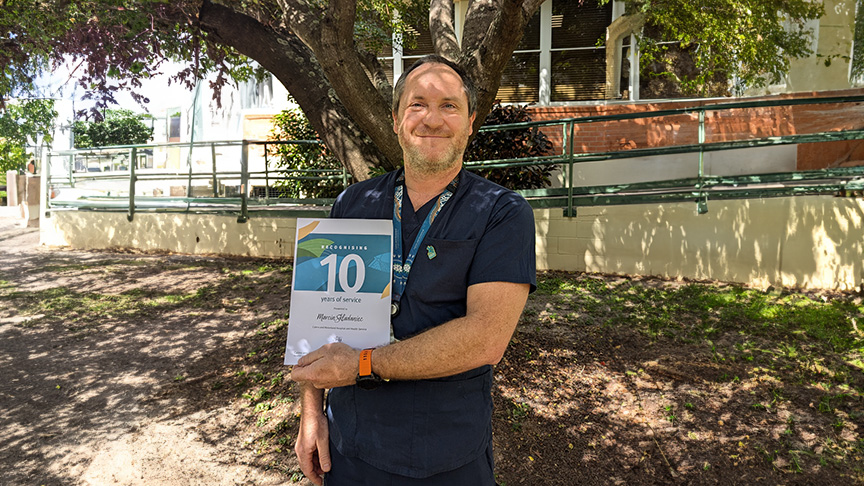 Staff member holding a certificate up outside of hospital