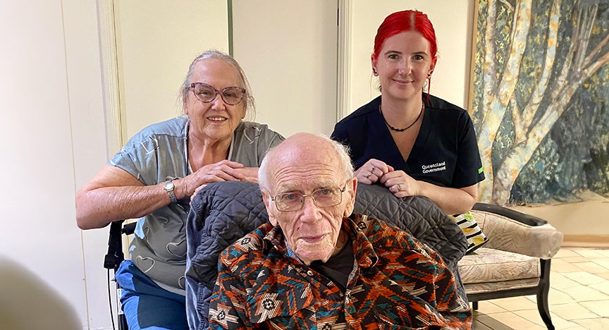 An elderly woman (Maggie Copp) and a young nurse with red hair (Registered Nurse Alisa Aldam) sitting behind an old man (Jim Copp)