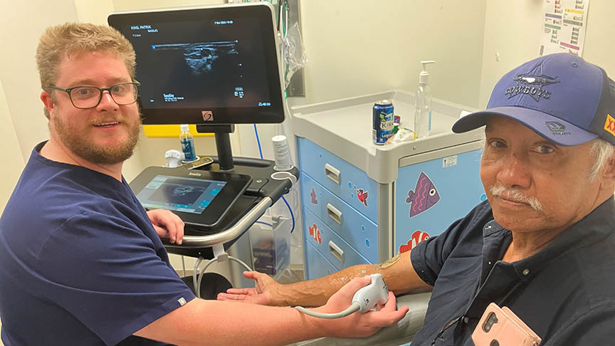 Male nurse (Shaun) using an ultrasound machine on another man's (Patrick) arm