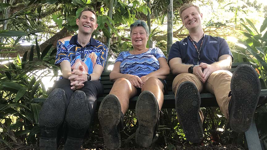 Two men and a woman sitting on a bench showing the bottom of their shoes to the camera