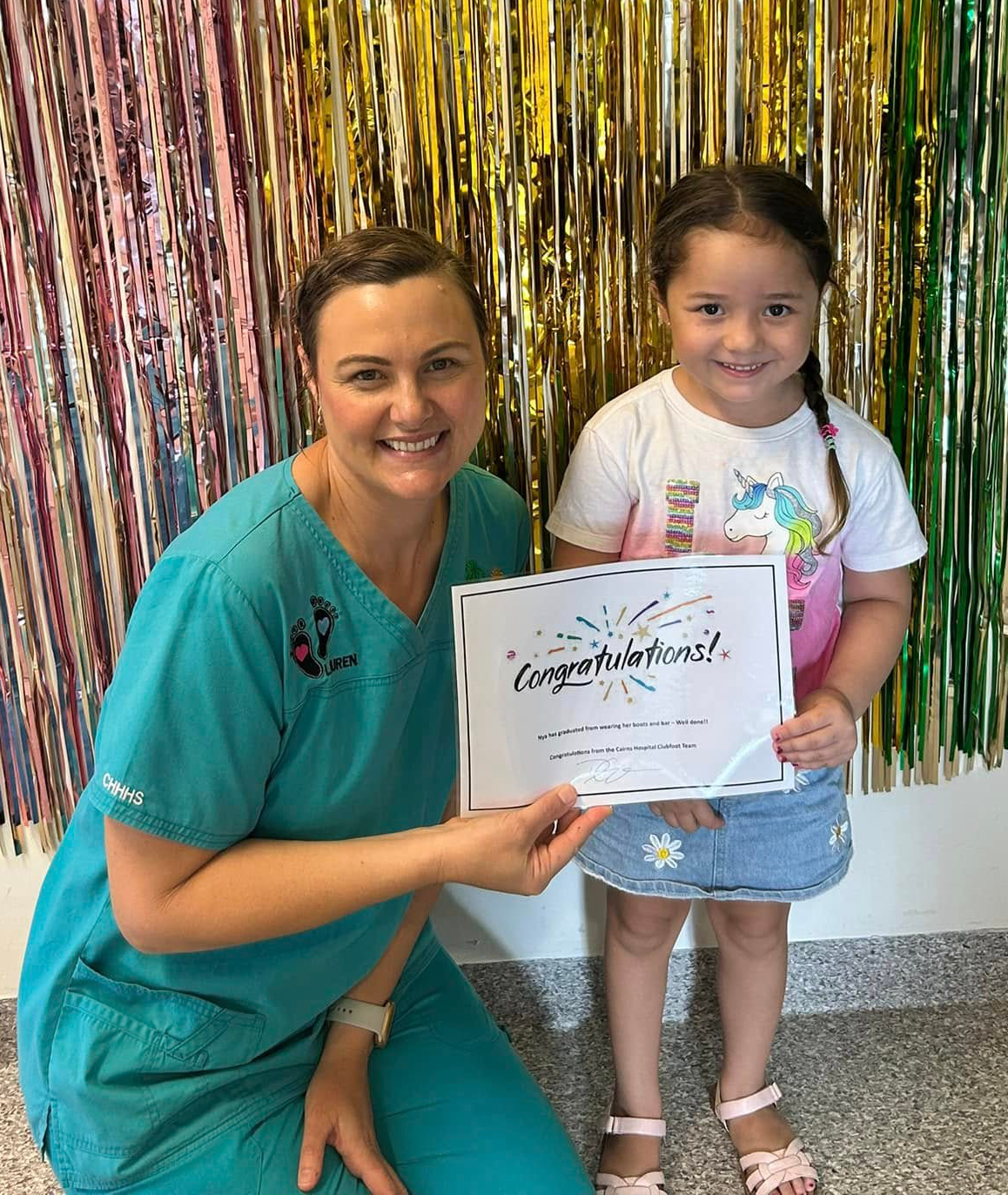 Nurse and little girl standing in front of glittery background holding a certificate and smiling