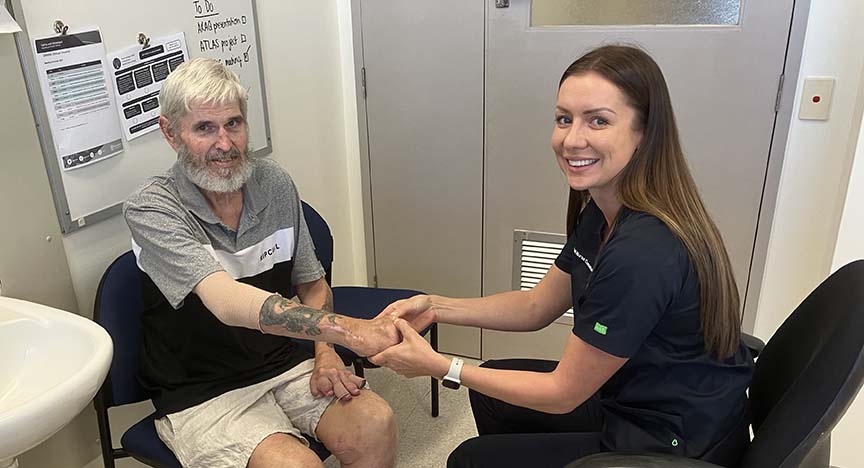 Woman (Clinical Nurse Consultant Sabina Schot) sitting in front of and holding a man's (Jason Turner) hand